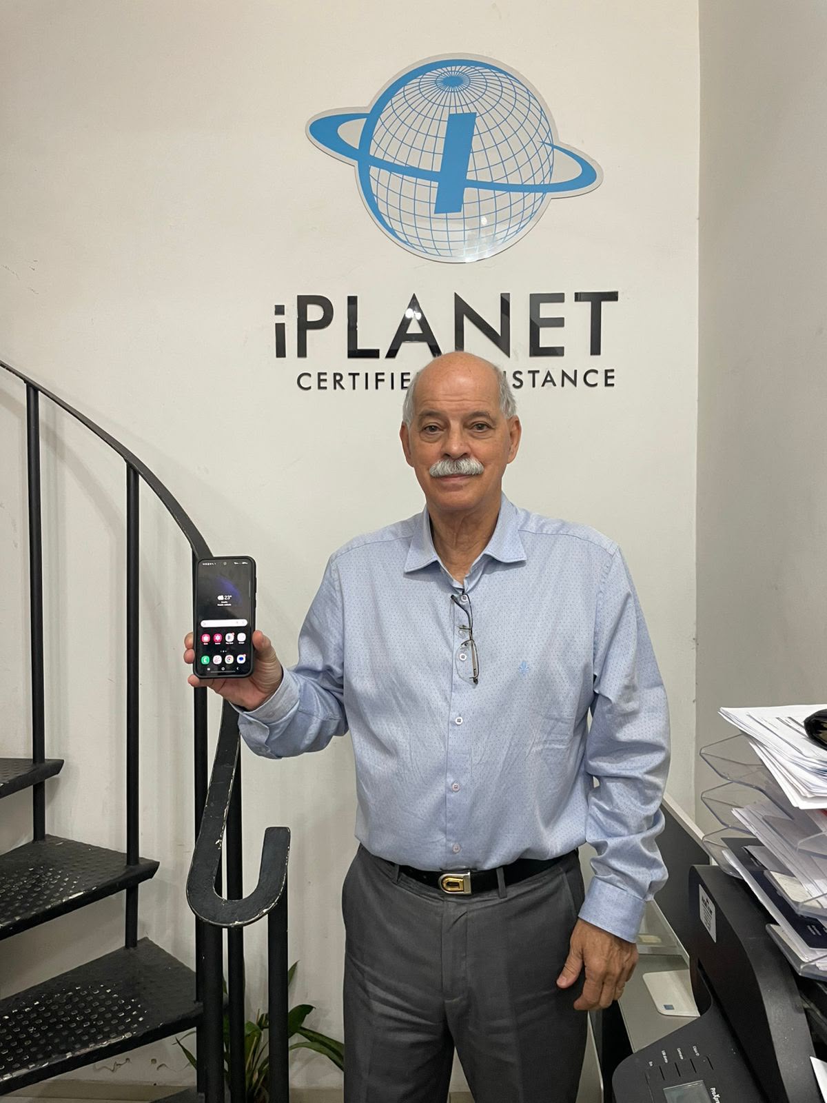 Cliente com o celular em frente ao logo da iPlanet Certified Assistance
