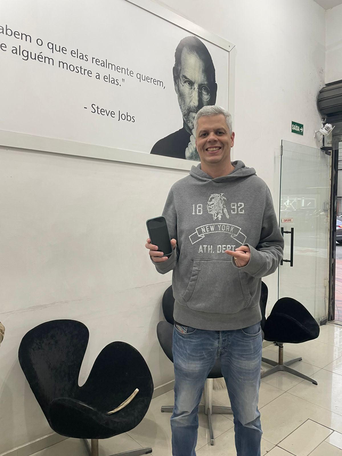 Cliente de moletom cinza com o celular na sala de espera da iPlanet